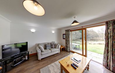 Living area with sliding patio doors leading to garden with view across the lambing field and loch.