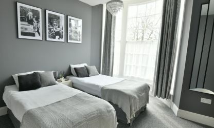 Stylish first floor bedroom with two single beds, large mirror, and en-suite bathroom