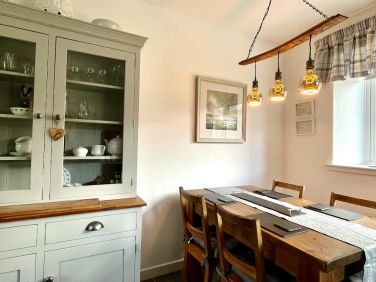 A well-equipped kitchen featuring a dresser, dining table, and unique whisky stave light fixtures.