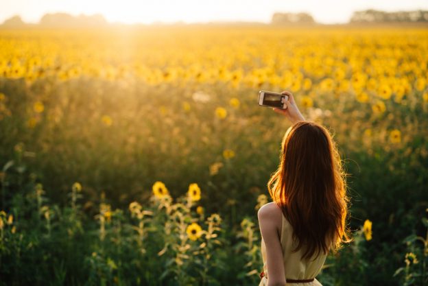 Lady taking a picture in bright sunshine of a field of sunflowers