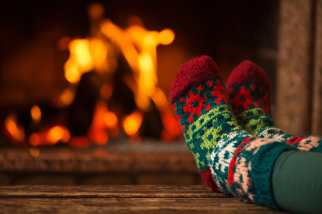 Feet in Christmas knitted socks in front of roaring fire
