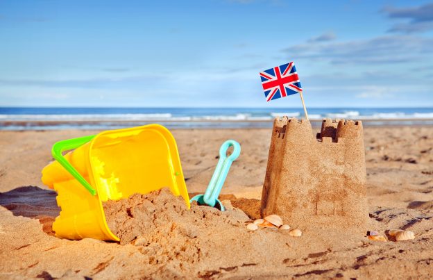 A sandscastle with Union Jack, yellow bucket and spade on a British beach.