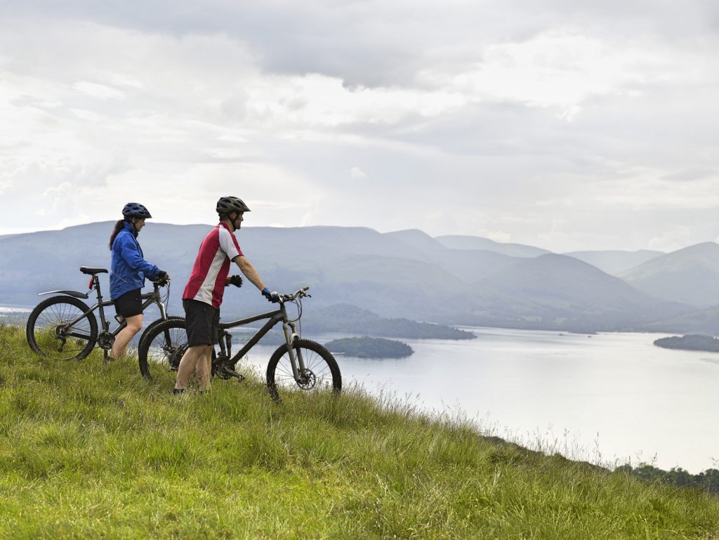 Girl and boy on mountain bikes looking over a large lake on a cloudy day