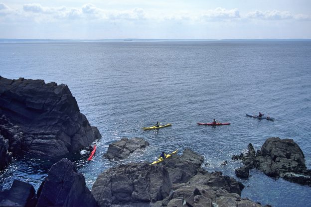 Kayakers paddling around rocks in the sea