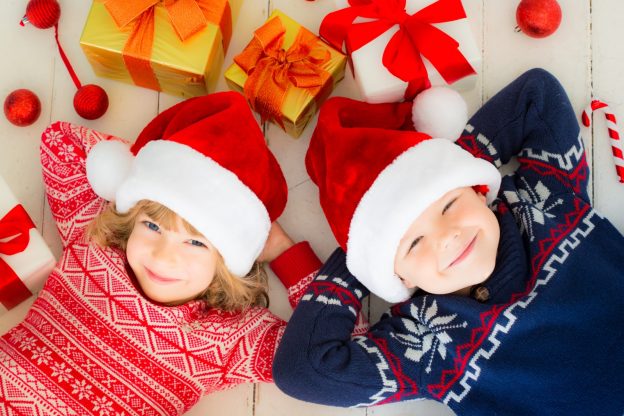 Small boy and girl laying amongst presents with Christmas Santa hats on