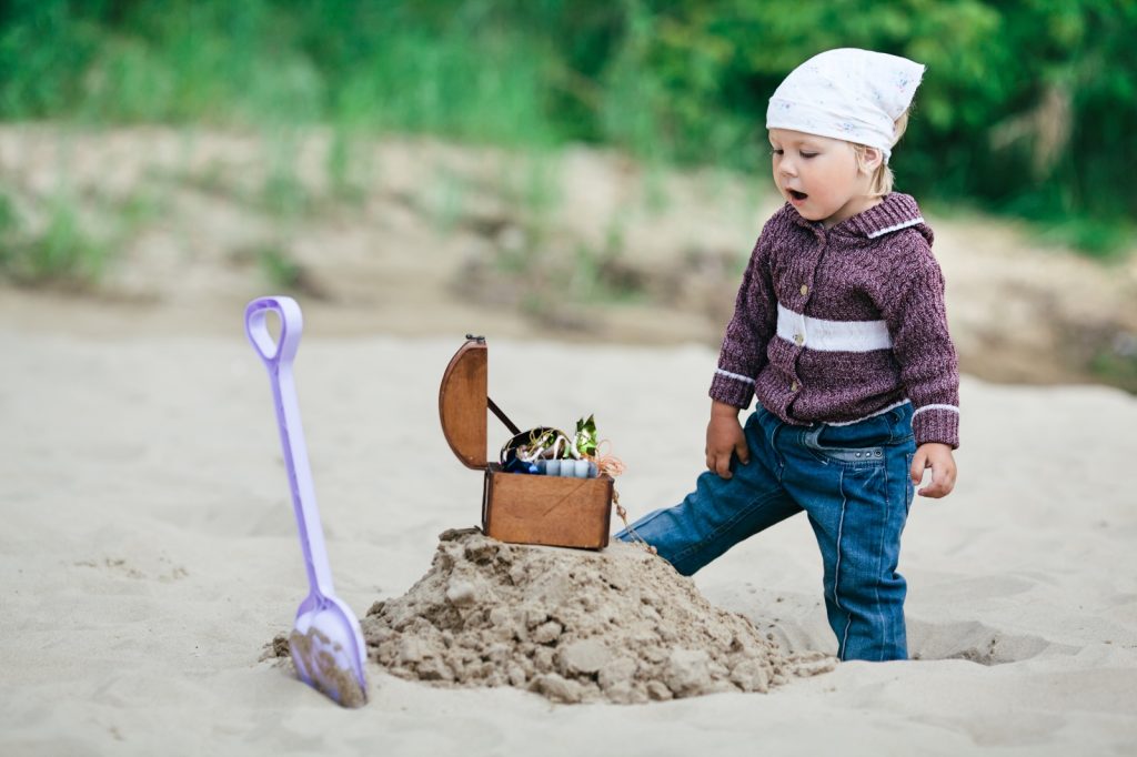 Child looking surprised at small treasure chest dug up on beach