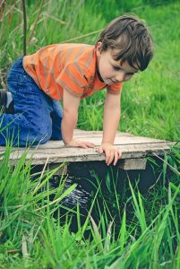 Little boy in orange stripy top and jeans looking over wooden bridge at the water