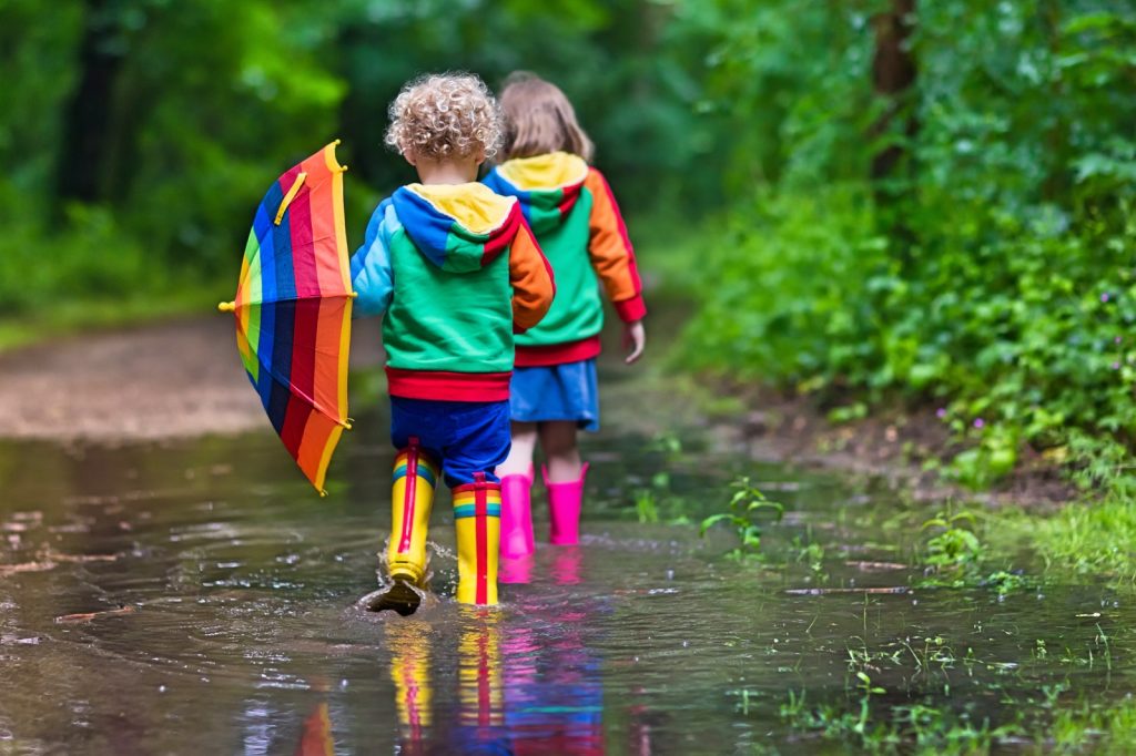 Little boy and girl in brightly coloured clothes and wellies with umbrella