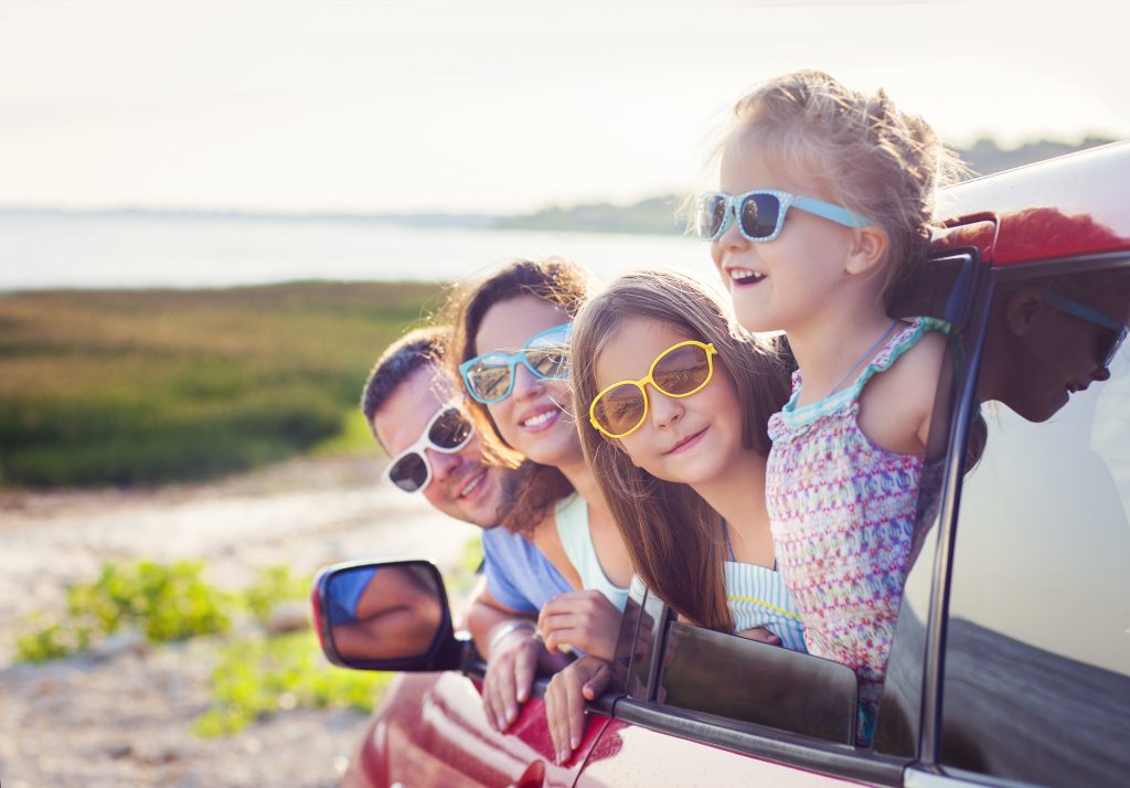 Family leaning out of the car window smiling with sun glasses on