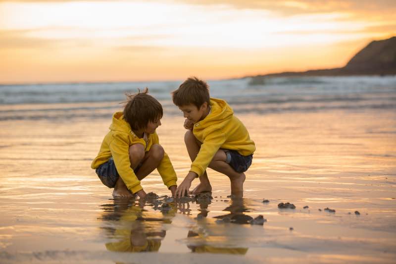 Two brothers building sandcastles on the beach at sunset