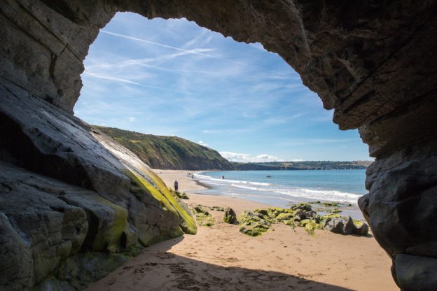 Looking through the opening of a cave out onto a sandy beach