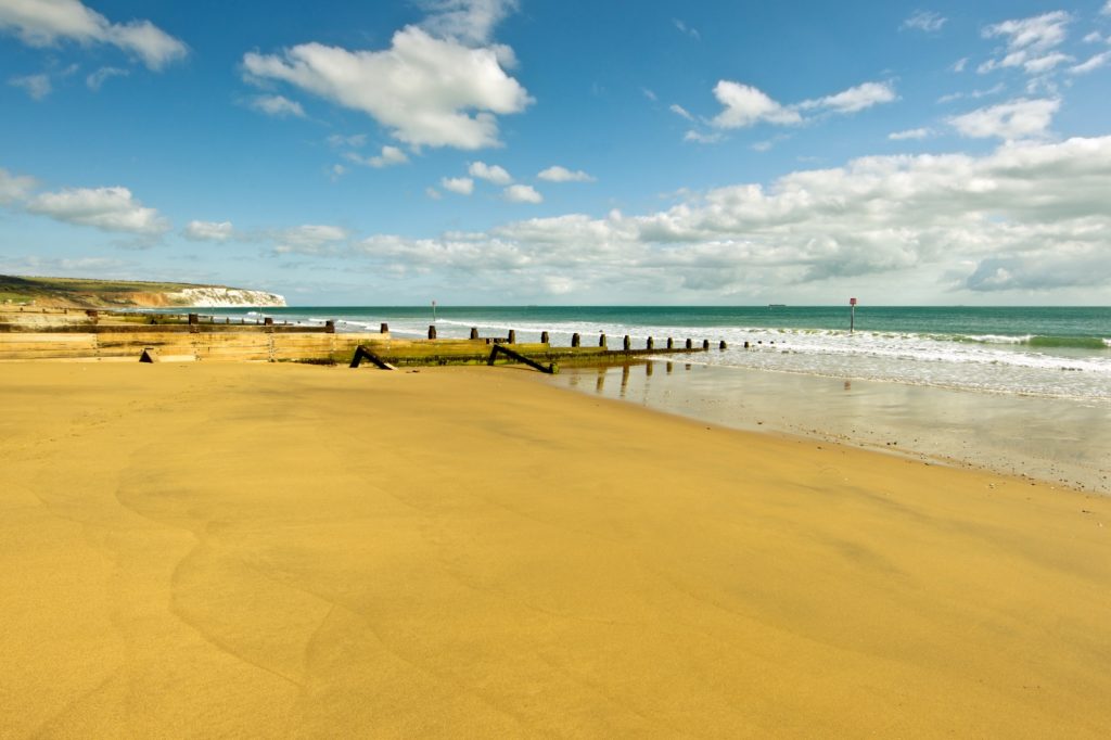Vast open golden beach on a sunny day with blue waves gently lapping at the shore line and wooden breakwaters