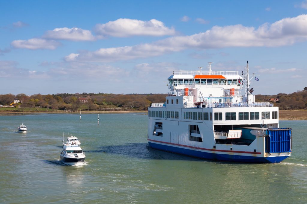 White & blue ferry with small boat alongside crossing the water of the Solent on sunny day with clouds in sky