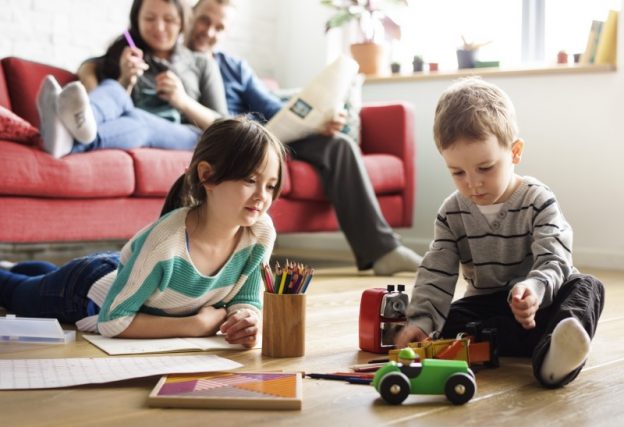 Children playing on the floor with colouring books while adults relax on sofa