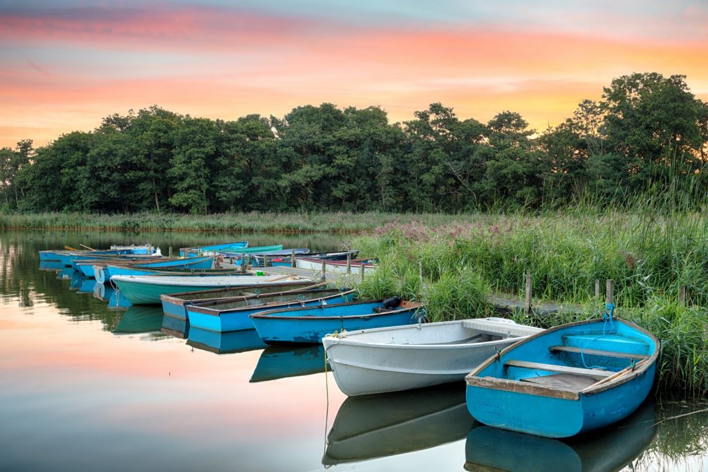 Blue and white rowing boats moored up on the river with trees and sun setting behind