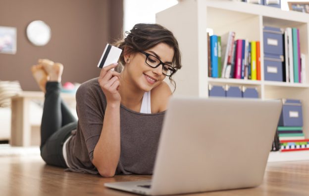 Women wearing glasses holding credit card, laying on floor in front of computer